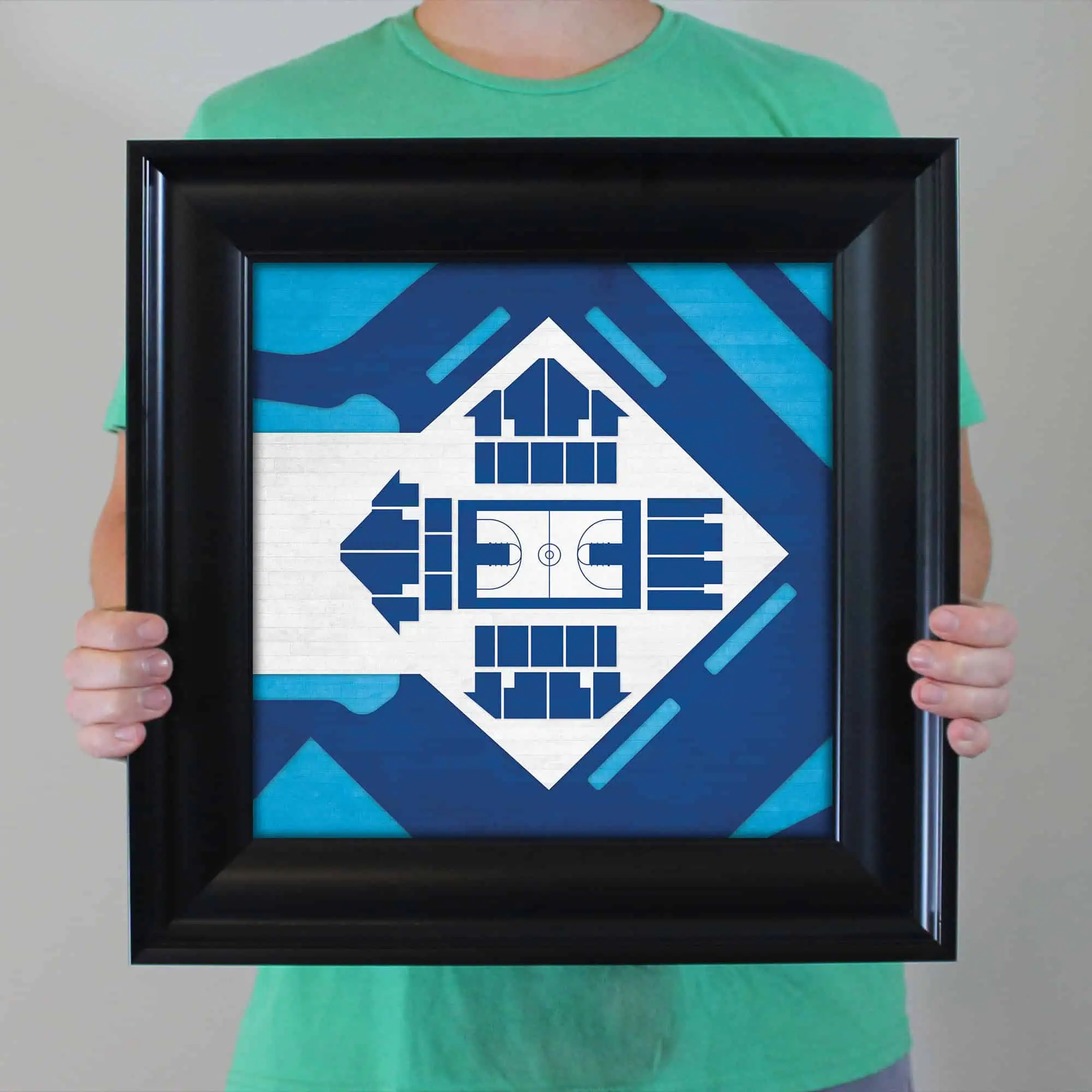 Hand holding framed football stadium artwork in blue tones, showcasing detailed arena design with seating, field, and surrounding abstract elements. Perfect for sports fans and decor enthusiasts.