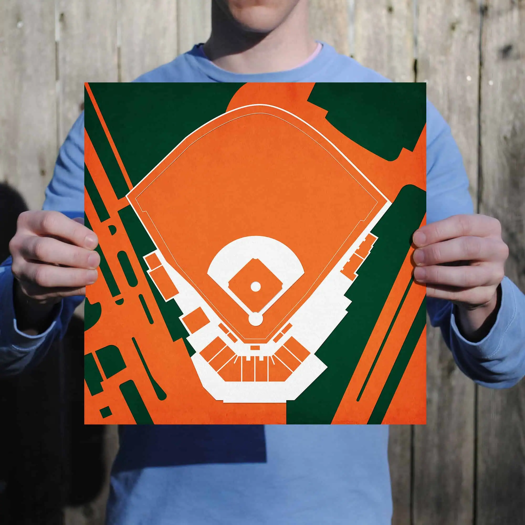 Vintage baseball field map with stadium seating, in orange, white, and green colors, held by a person in a blue shirt outdoors.