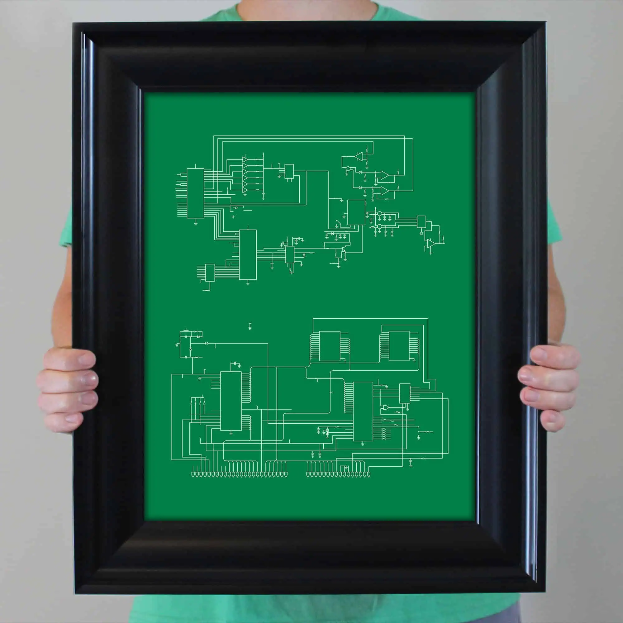 Circuit diagram of electronic components on green background, held in black frame by person in green shirt.