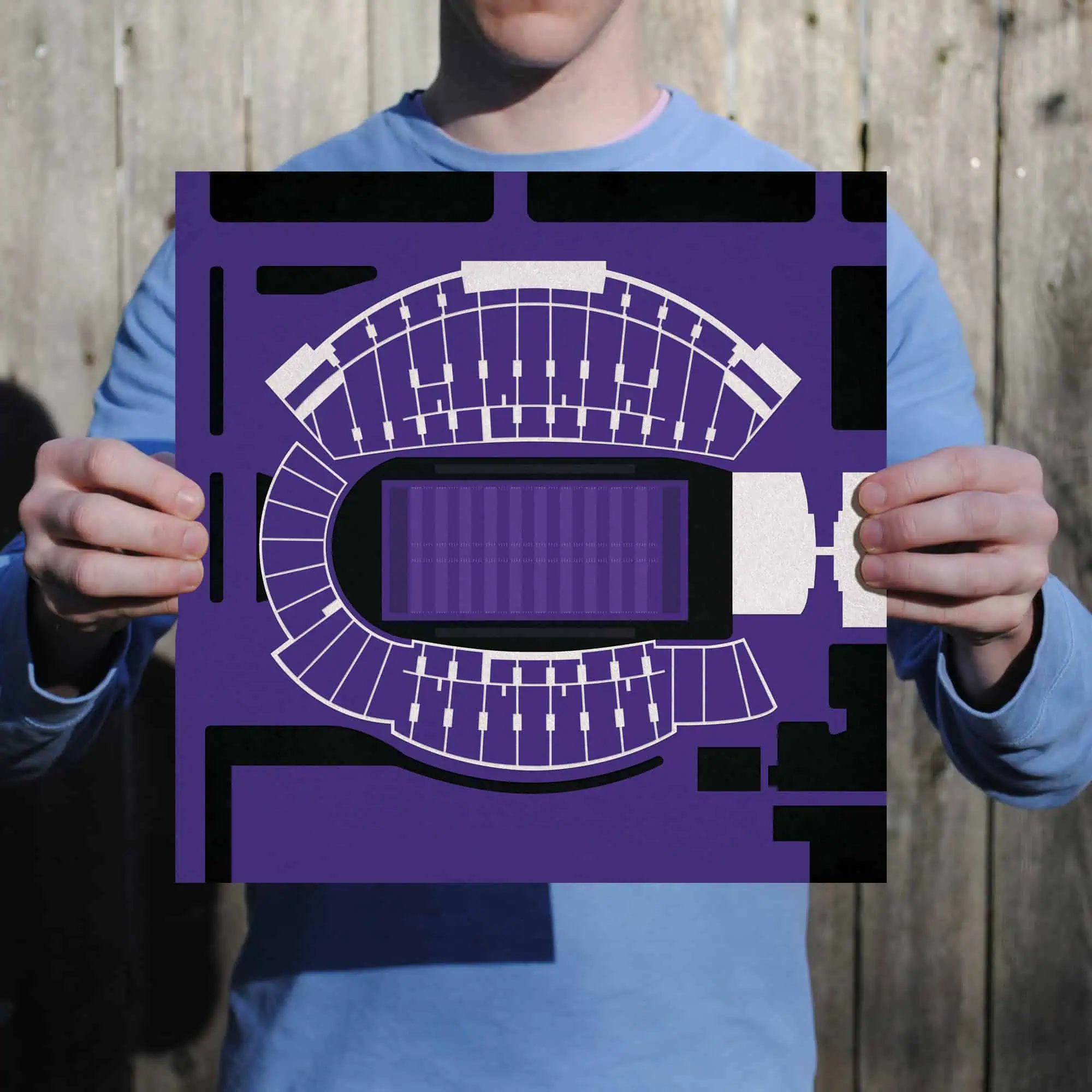 A person holding a purple stadium seating chart or seating plan, displayed outdoors against a wooden fence background, showcasing event venue layout and seating arrangements.