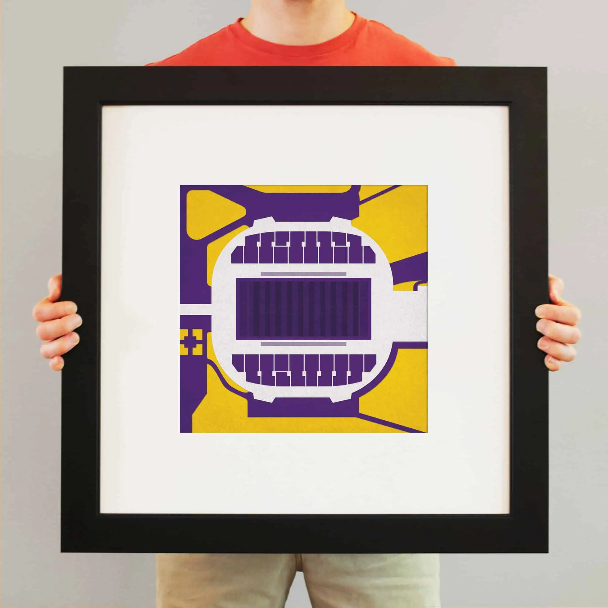 Colorful abstract art print of a stadium or arena with purple, yellow, and white geometric shapes, framed and displayed by an individual.