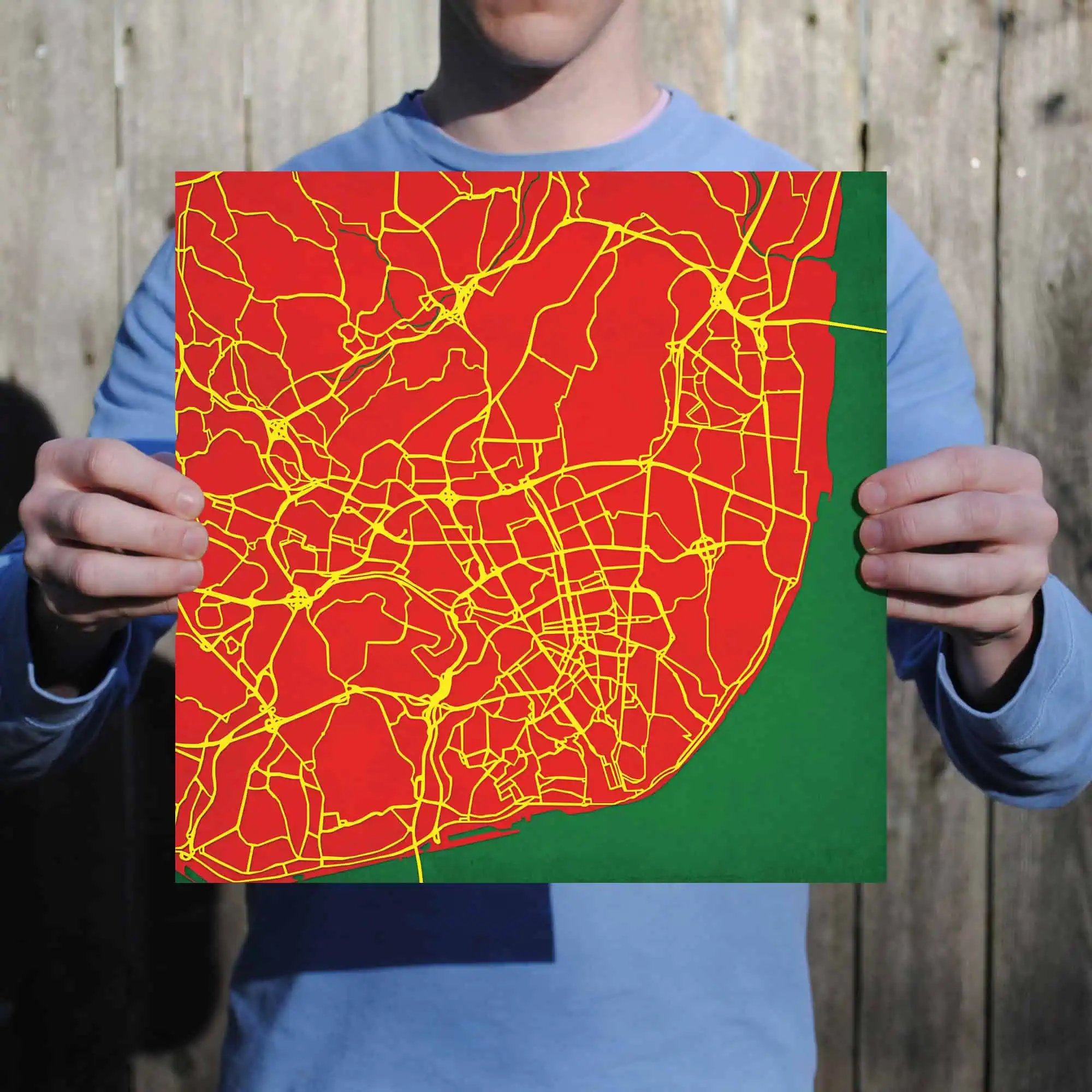 Detailed city street map with yellow roads on a bold red background, held by a person in front of a wooden fence, emphasizing urban navigation and cartography.