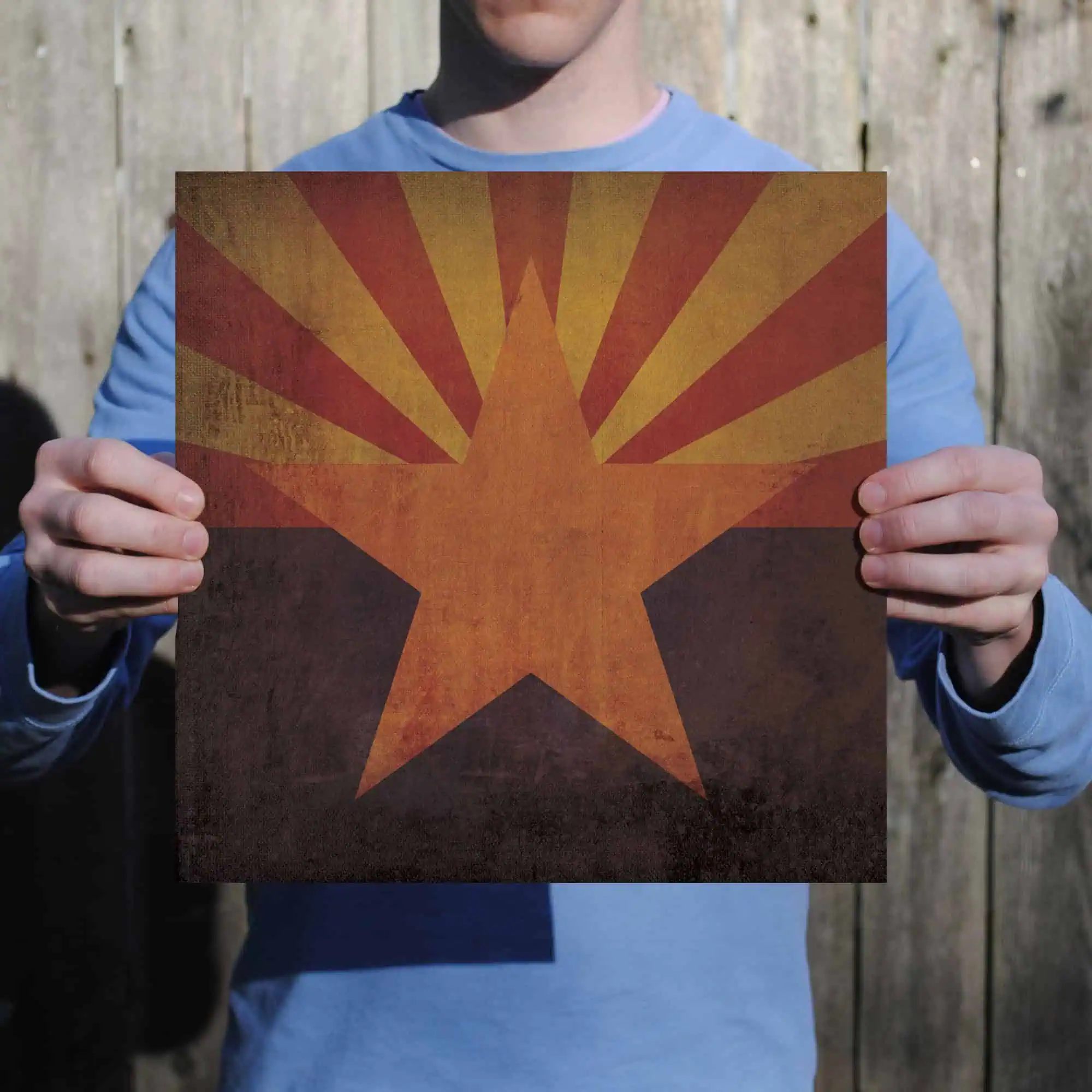 Vintage Arizona State Flag, retro style with a textured look, held by a person against a wooden fence background. Ideal for state pride, Arizona souvenirs, or vintage design themes.