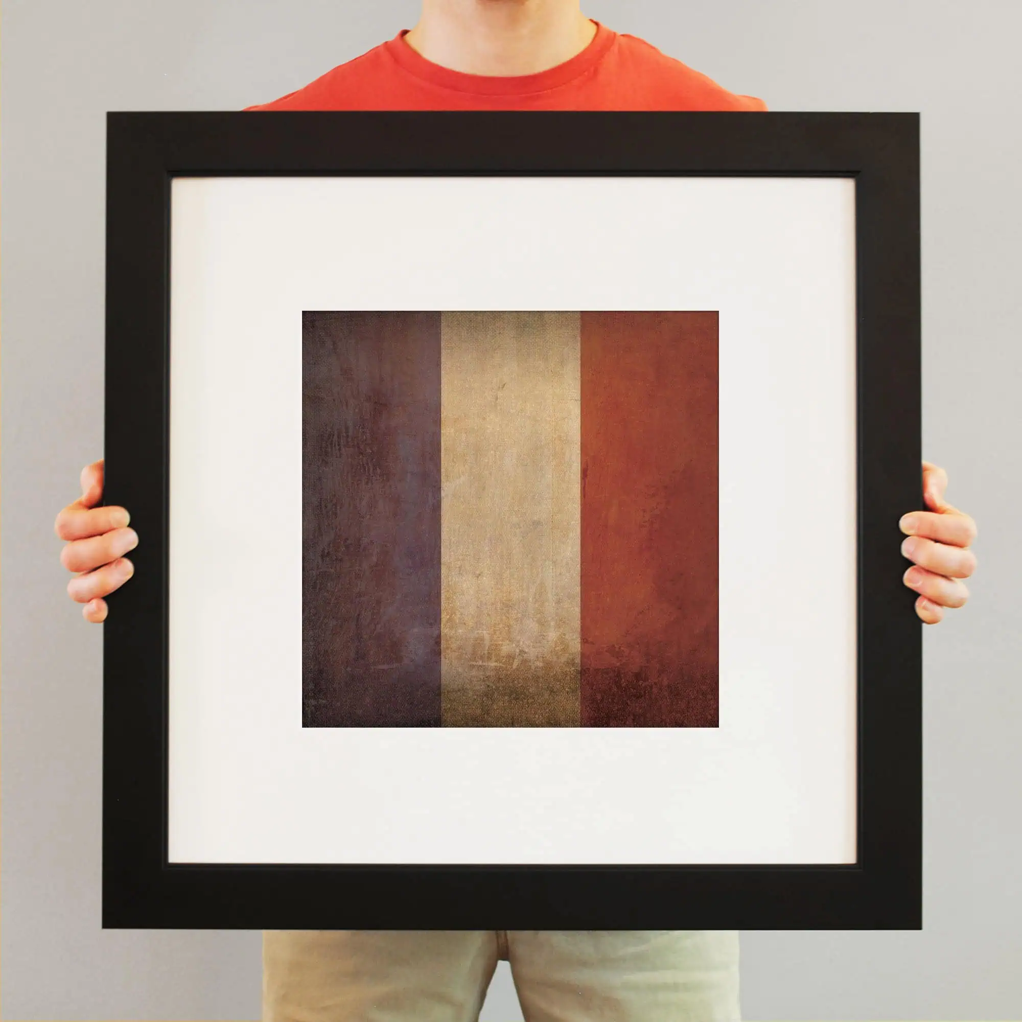 A framed abstract artwork featuring vertical gradient stripes in navy blue, beige, and rust red, held by a person wearing a red shirt, emphasizing art collection and framing services.