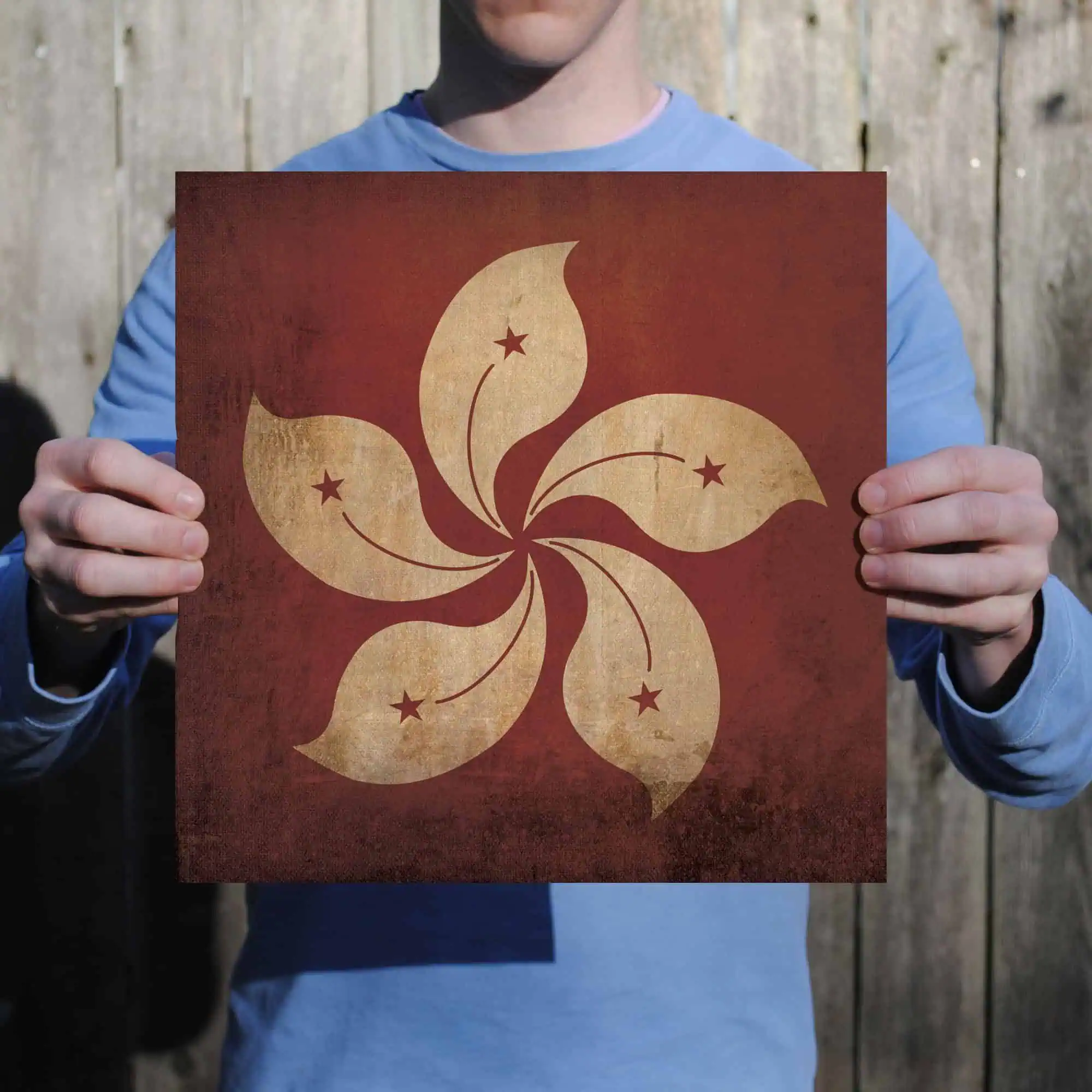 Hong Kong flag design print, vintage style, with five stars and flower motif, held by a person in a blue jacket against a wooden background.