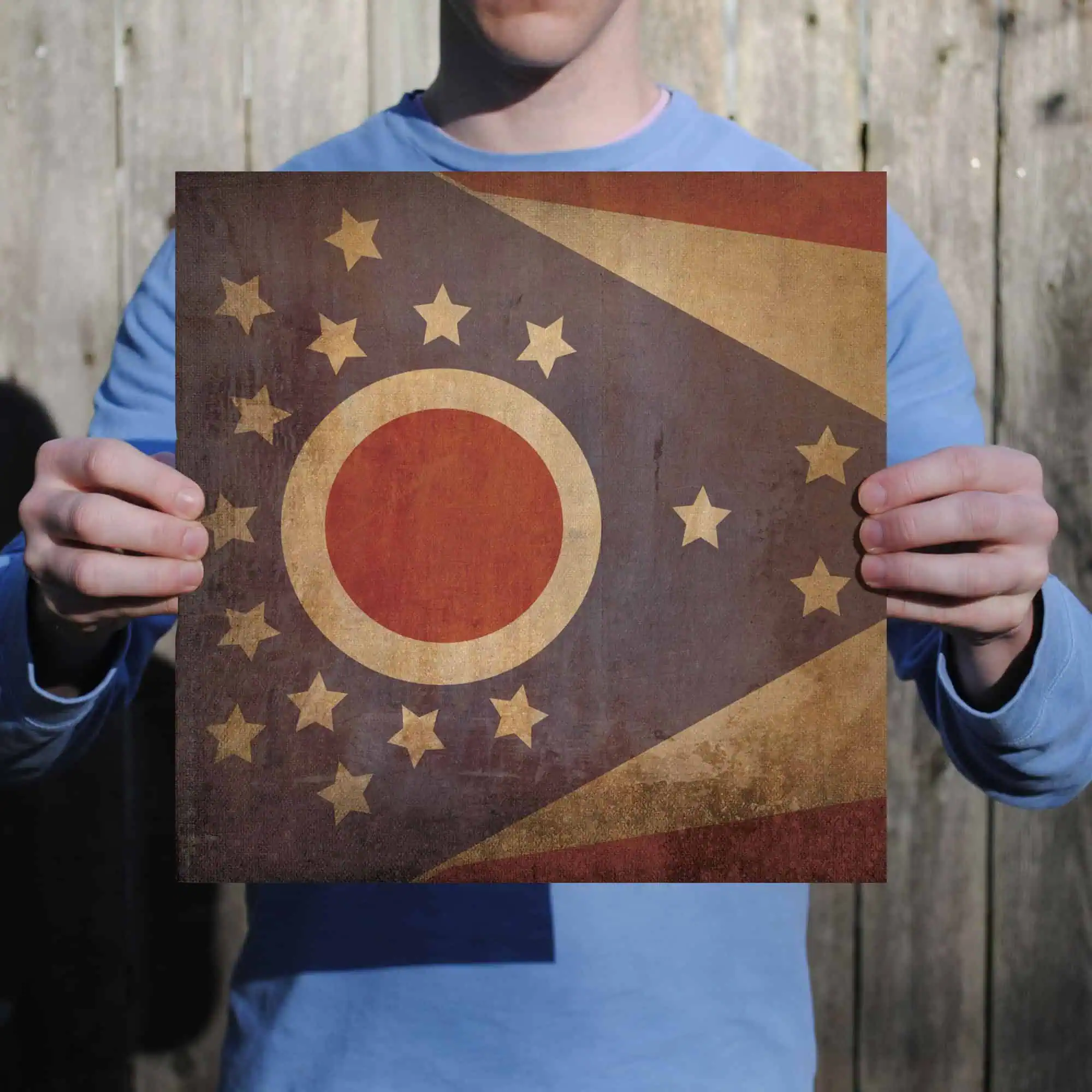 Vintage flag of Ohio, featuring a rusty, distressed appearance with stars and circular emblem, displayed by a person outdoors.