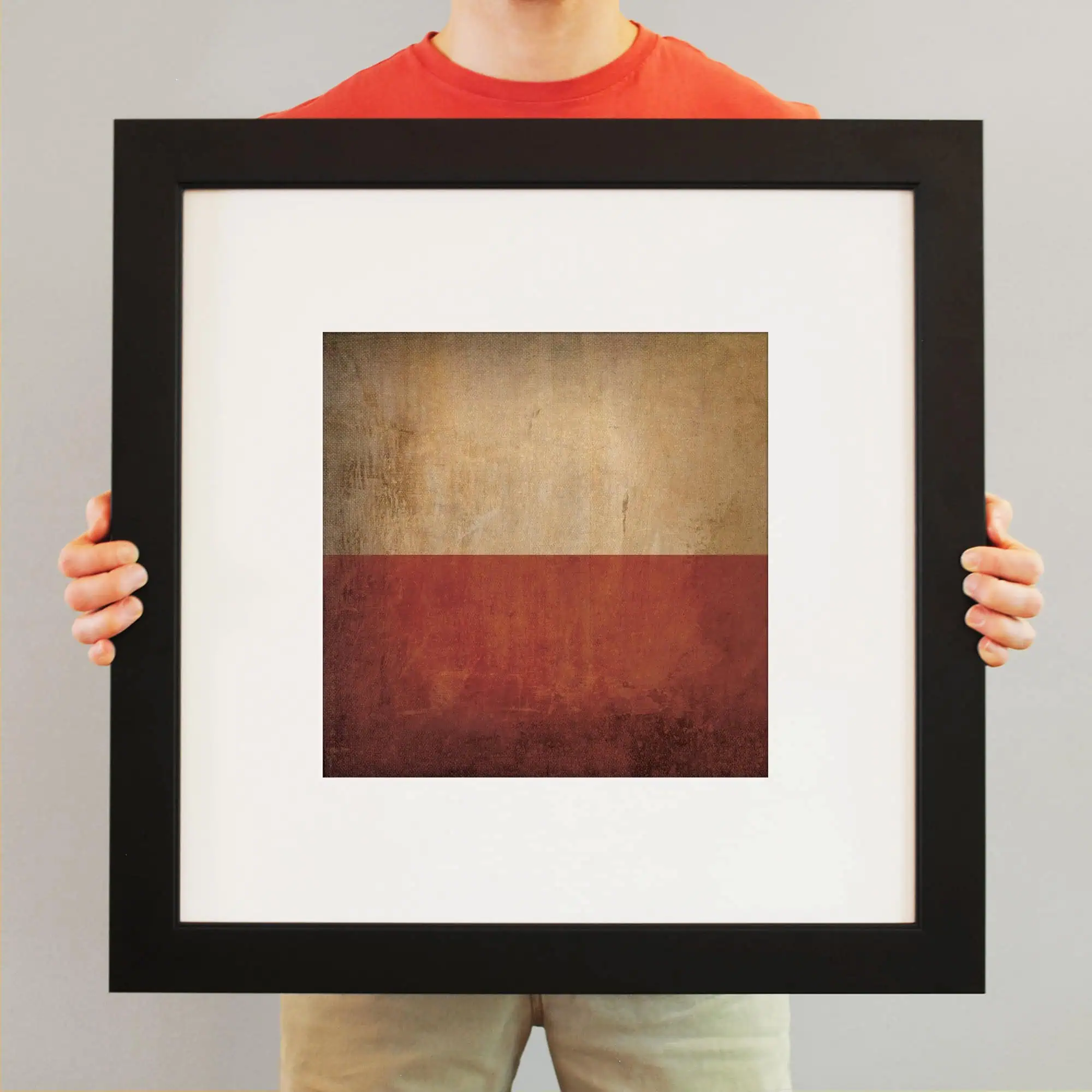 A person holding a framed abstract artwork with a textured, earthy color palette in a modern gallery setting.