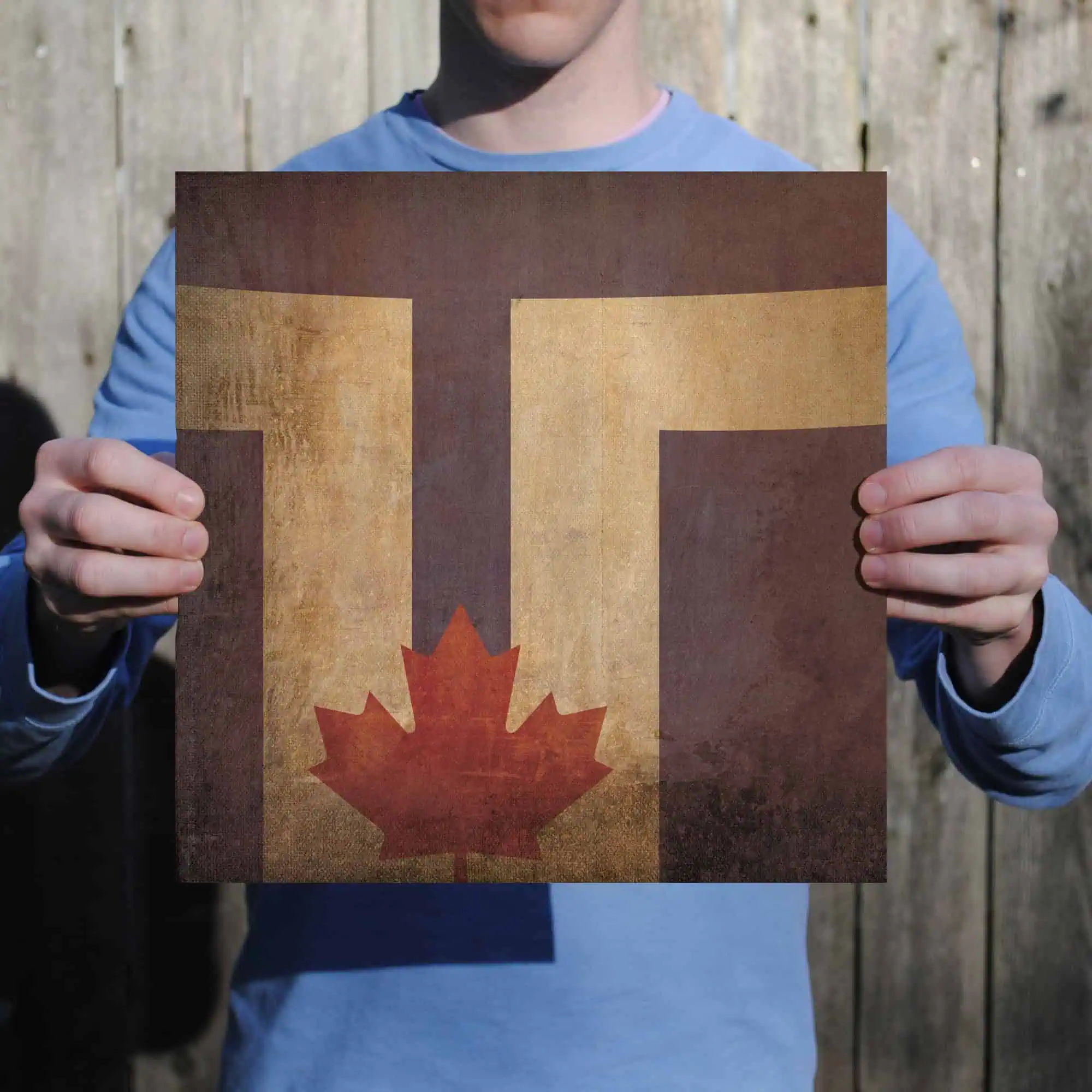 Flag of Canada with maple leaf design and vintage textured background, held by a person outdoors in front of a wooden fence, symbolizing travel, exploration, or Canadian identity.