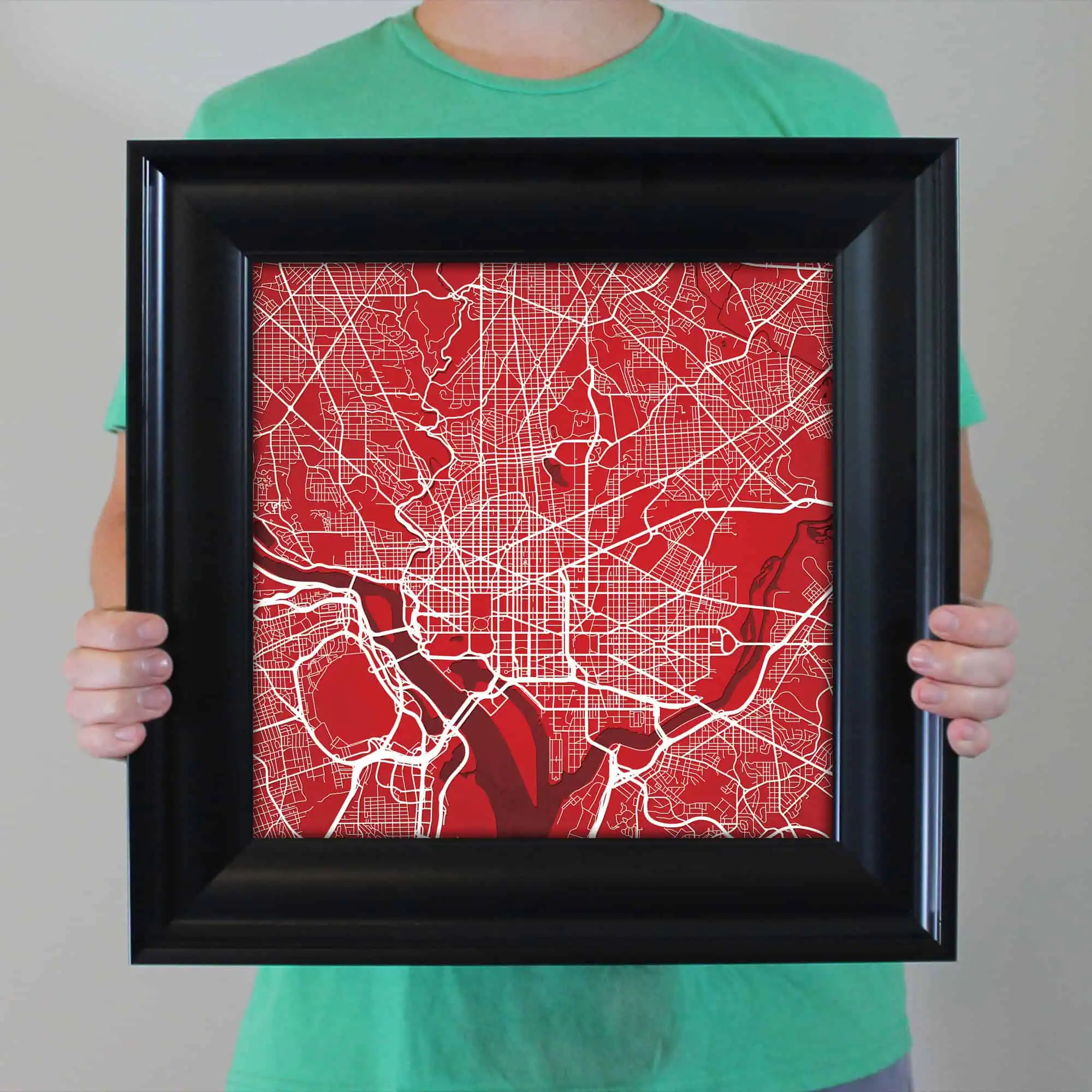 Detailed city map artwork with a vibrant red background and white street lines, framed and held by a person in a green shirt, ideal for travel, navigation, or decor enthusiasts.