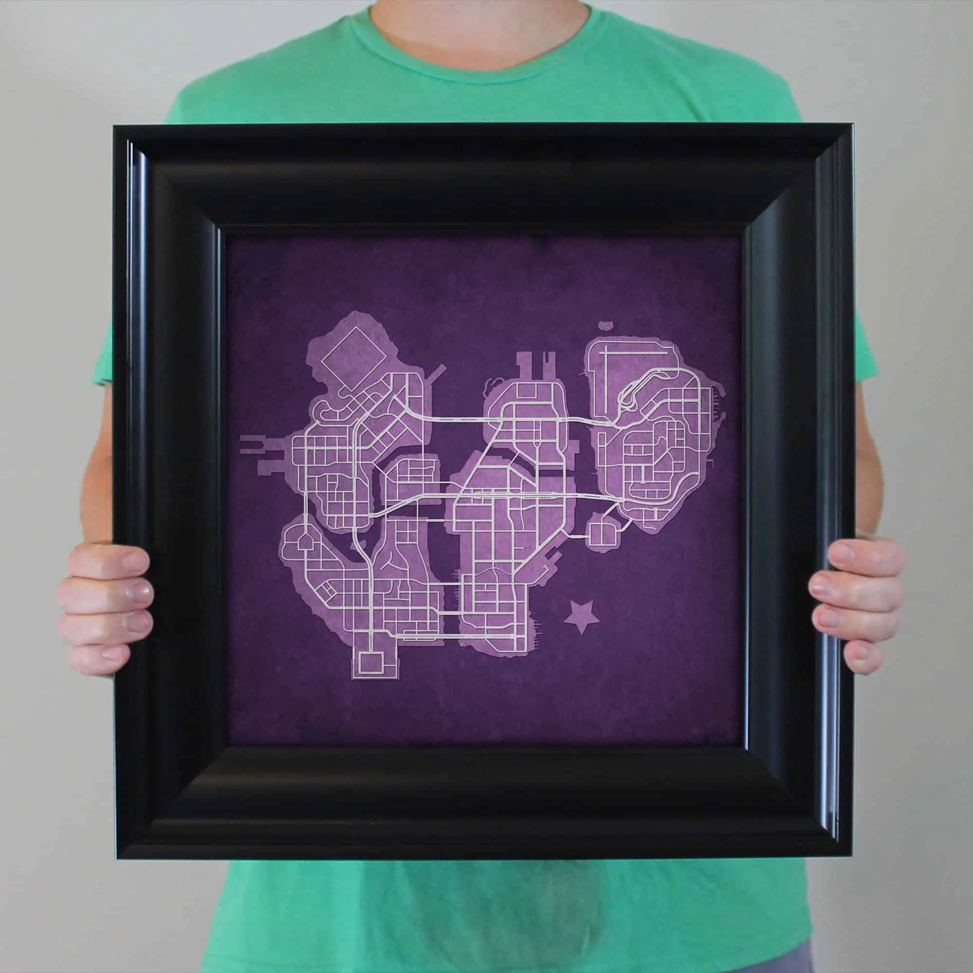 Detailed map art of a city printed on purple paper, held in a black frame by a person wearing a green shirt. Perfect for wall decor or navigation enthusiasts.