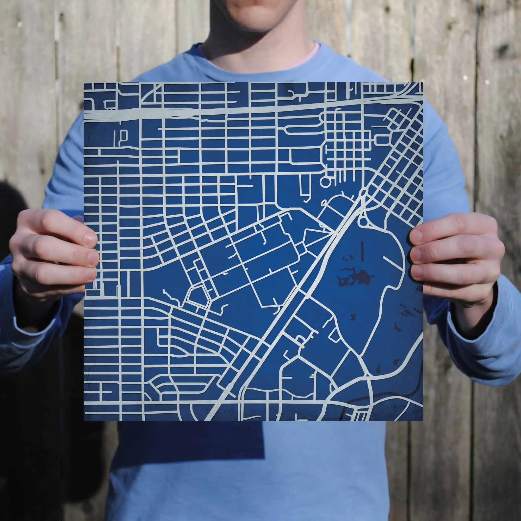 Detailed city street map held by a person in front of a wooden fence, showcasing urban navigation and map art, ideal for travel planning and geographic exploration.