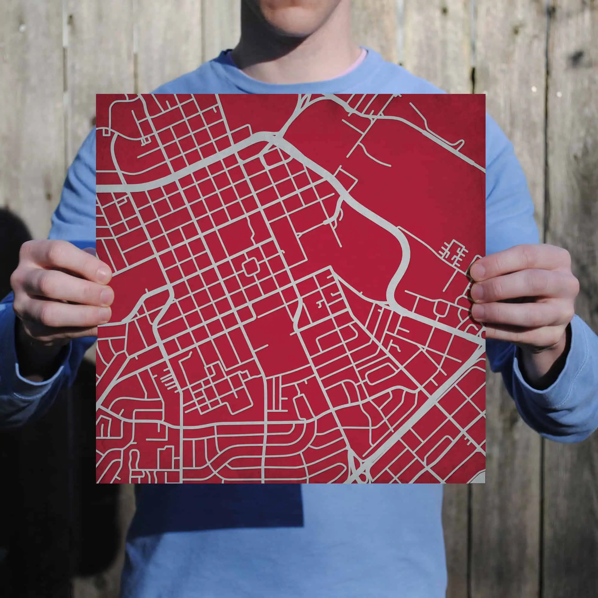 Detailed city street map with grid layout, held by a person in front of a wooden fence. Perfect for navigation, travel planning, and urban exploration.