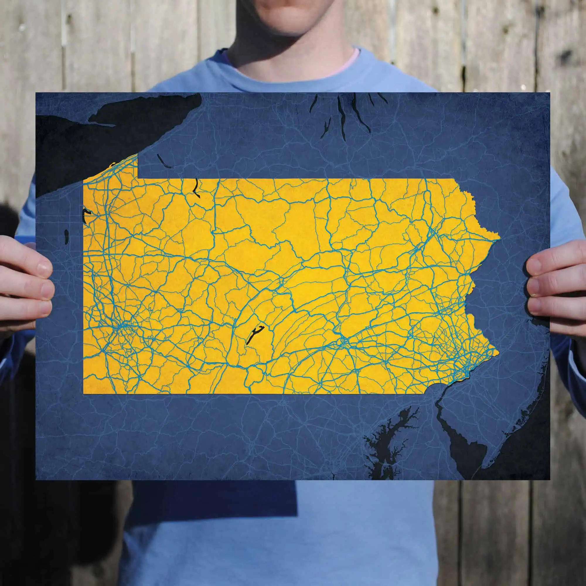 Detailed map of North Carolina with road networks, held by a person in front of a wooden fence.