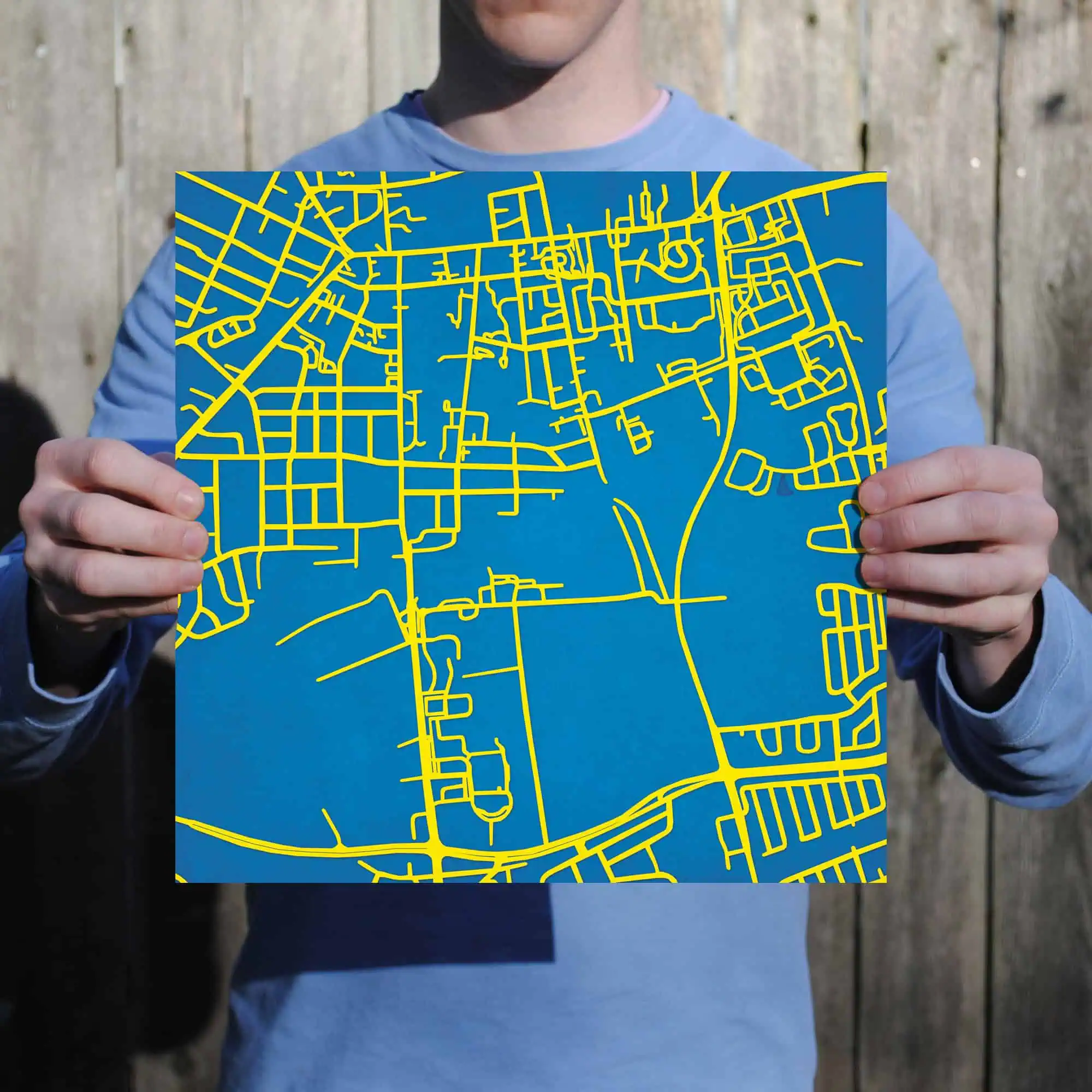 Colorful city street map with yellow lines on a blue background, held by a person in front of a wooden fence. Perfect for travel, navigation, and mapping enthusiasts.