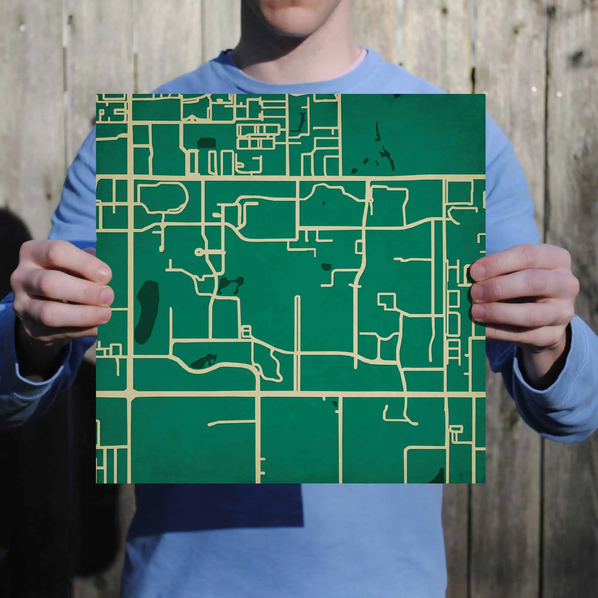A person holding a green city map for navigation, outdoors with a wooden fence in the background. Perfect for travel, hiking, or exploring urban areas with detailed maps.