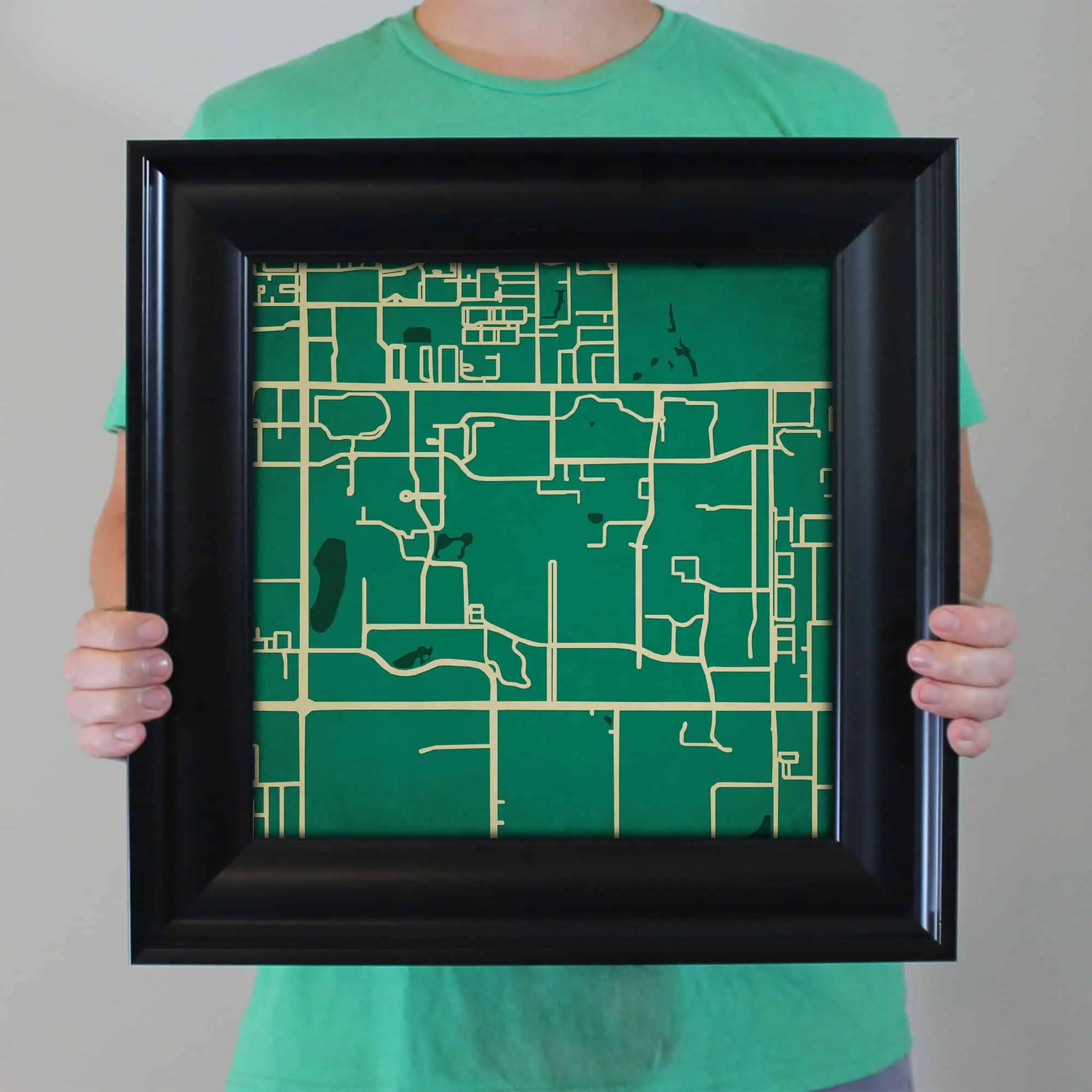 A person holding a framed map artwork featuring simplified street layout design, perfect for home or office decor. High-quality map print with bold black frame, ideal for travel, navigation, and geography enthusiasts.