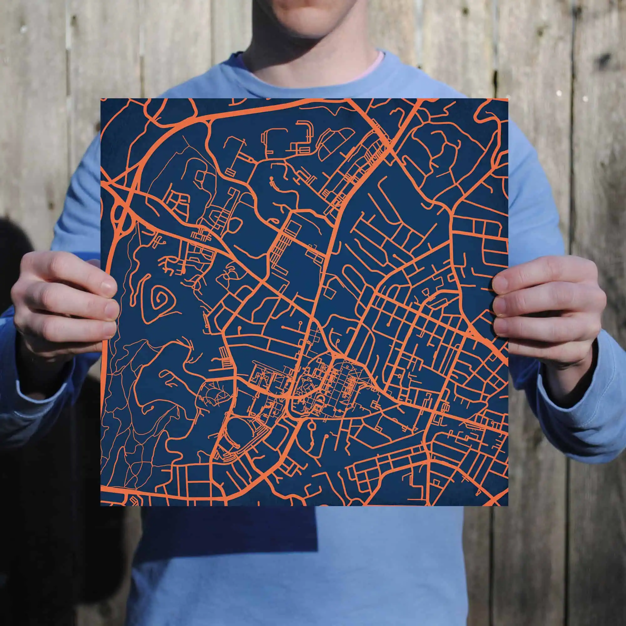 Detailed city street map with orange lines on a navy background, held by a person in blue clothing, showcasing cartography, navigation, and urban planning.
