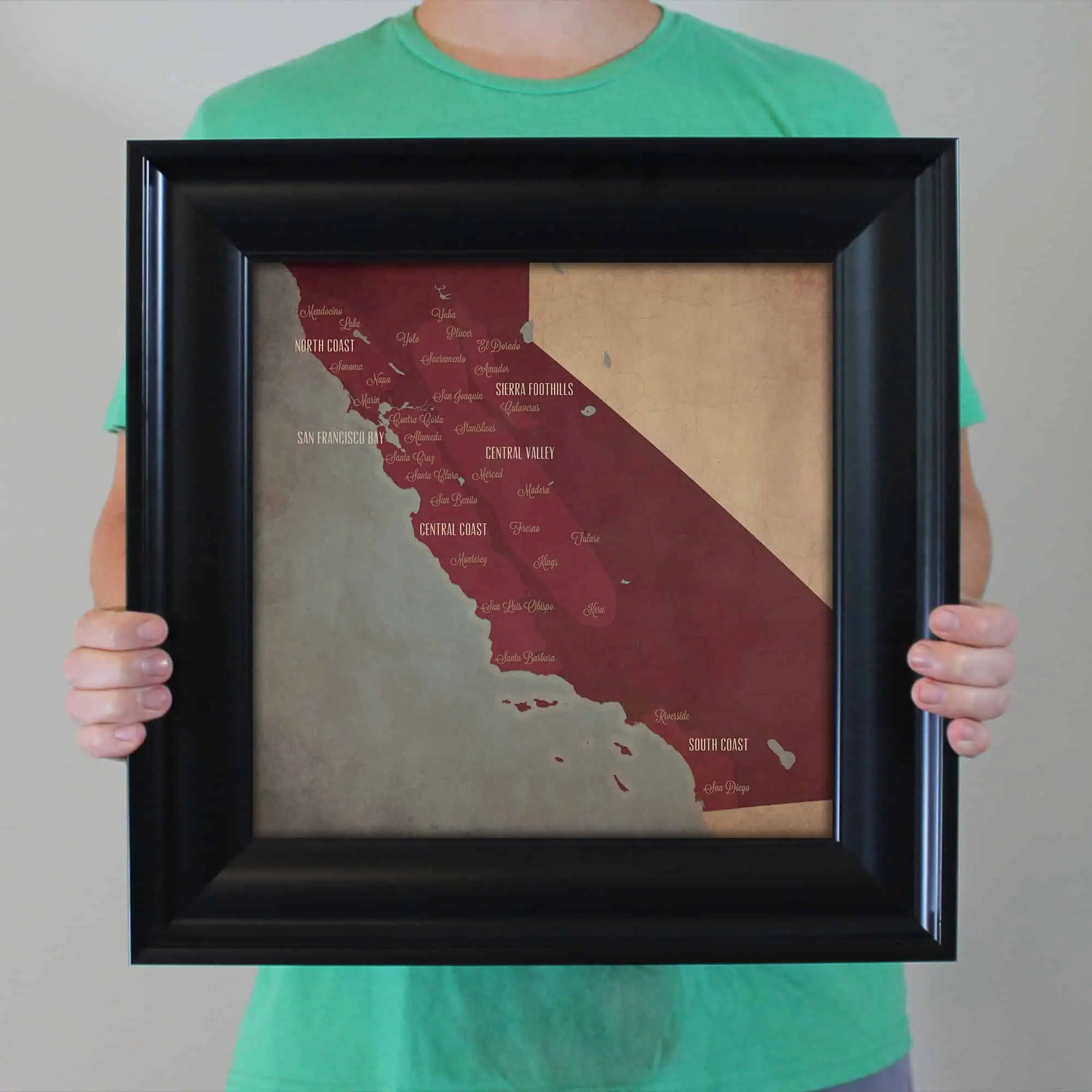 Vibrant historical map of California with regional labels, held in a black frame by a person wearing a green shirt, showcasing geographic regions like North Coast, Central Valley, and South Coast, suitable for educational and travel purposes.