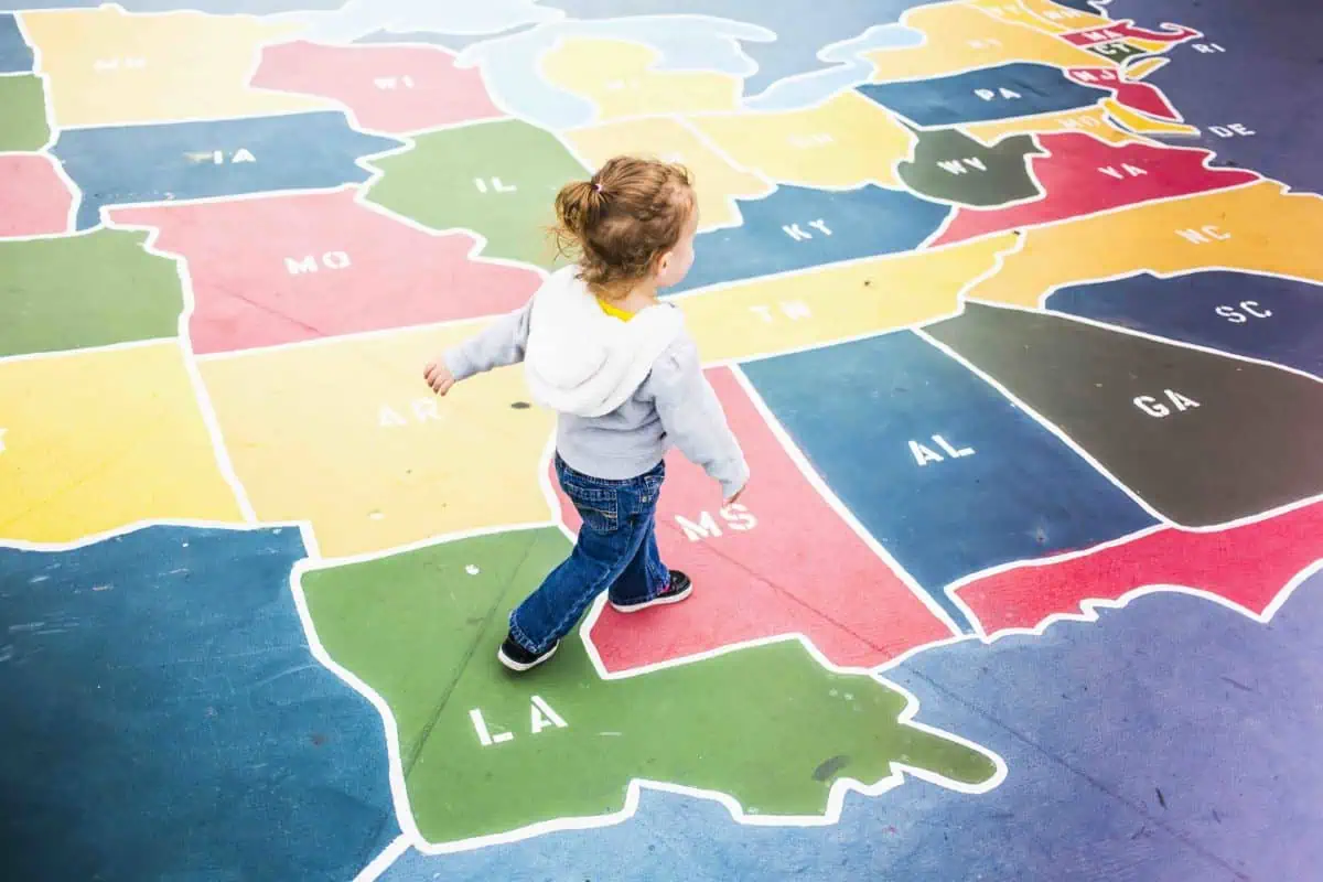 Colorful US map painted on pavement with a child walking on it, emphasizing geography and educational maps.
