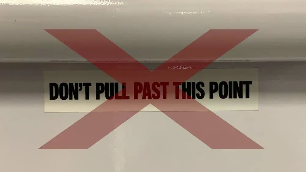 DON'T PULL PAST THIS POINT warning sign in bold black and red letters on a beige background, installed on a wall.